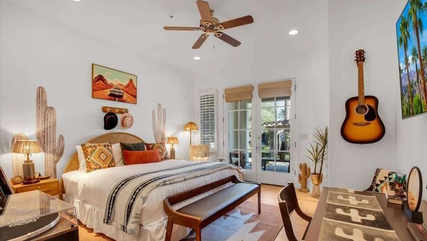 Une chambre à coucher avec un lit, un ventilateur de plafond, une guitare et un cactus accroché au mur.