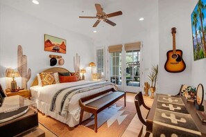 A bedroom with a bed, a ceiling fan, a guitar, and a cactus on the wall. - Desert Daydream B | Studio Legacy Villa (La Quinta)