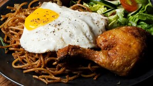 A plate of food with noodles, a fried egg, a fried chicken leg, and a side salad. - La Nusa Penida Homestay (Penida Island)