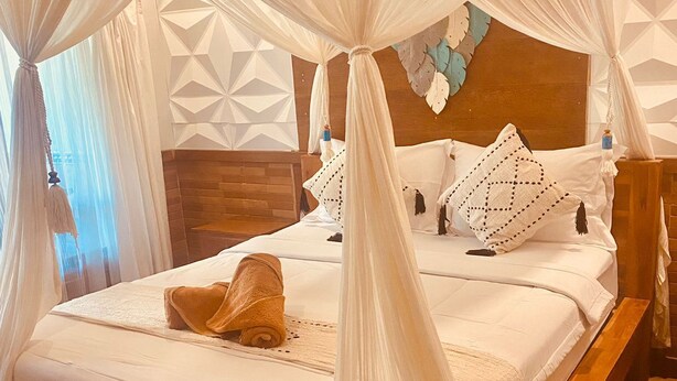 A bed with a canopy, a wooden headboard, and a geometric wall design. - La Nusa Penida Homestay (Penida Island)