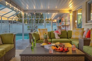 An outdoor patio area with a pool, green sofas, and a table with drinks and fruit. - Heated saltwater pool + bubbling hot tub + cozy massage chair (Bradenton)