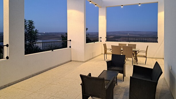 A spacious balcony with a clear view of the landscape, furnished with wicker chairs and a table, and illuminated by ceiling lights. - Mount Tabor Home by Sea N' Rent (Emek Izrael)