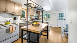 Une cuisine avec des meubles de rangement en bois, un fourneau blanc, un étendoir suspendu et une table à manger ornée de fruits.