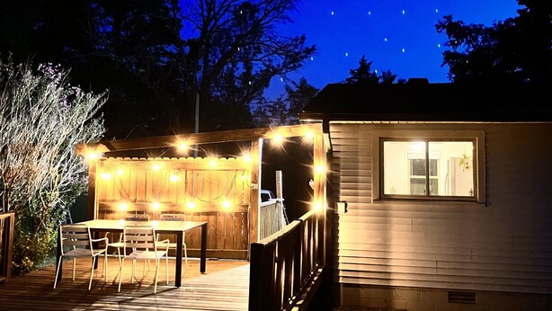 A wooden deck with a table and chairs, a small building with a window, and string lights. - Acre Inn- private countryside home south of Nashville, 15 min to Spring Hill (Spring Hill)