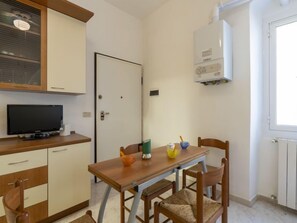 A small, clean room with a wooden dining table, two chairs, a TV, a white door, and a window. - Apartment Piero by Interhome (Sanremo)
