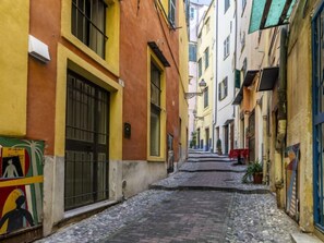 A narrow cobblestone street flanked by colorful buildings with barred windows and doors. - Apartment Piero by Interhome (Sanremo)