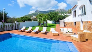 A swimming pool with lounge chairs, a white building with stone walls, and a mountainous backdrop. - Vacation home Agave by Interhome (Calpe/Calp)