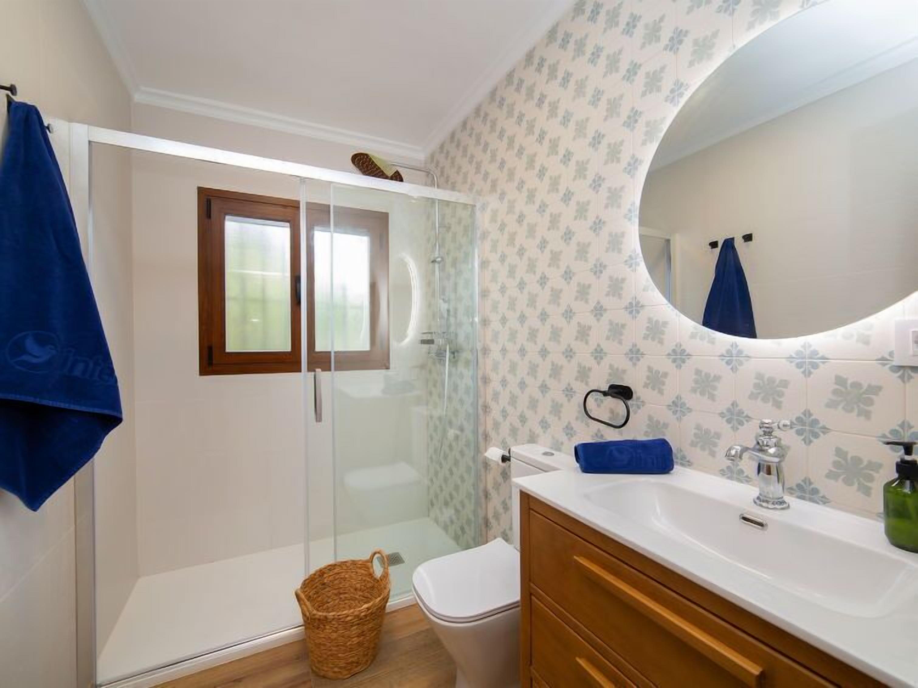 A bathroom with a glass-enclosed shower, a white toilet, a wooden vanity with a sink, and a mirror above the vanity.