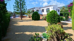 A white villa with a sandy courtyard, surrounded by lush greenery and a clear blue sky. - Vacation home Agave by Interhome (Calpe/Calp)