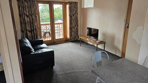 A living room with a sofa, a TV on a wooden table, and a balcony with curtains. - Cairns holiday unit apartment kitchen aircon wifi near esplanade and hospital (Cairns North)