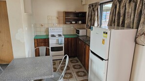 A compact kitchen with a stove, microwave, and refrigerator. There is a dining table with chairs, and the floor has patterned tiles. - Cairns holiday unit apartment kitchen aircon wifi near esplanade and hospital (Cairns North)