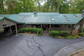 A rustic lodge with a green metal roof, a covered porch, and a stone chimney.