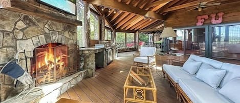 Una amplia zona de estar al aire libre con chimenea de piedra, muebles de madera y un ventilador de techo.