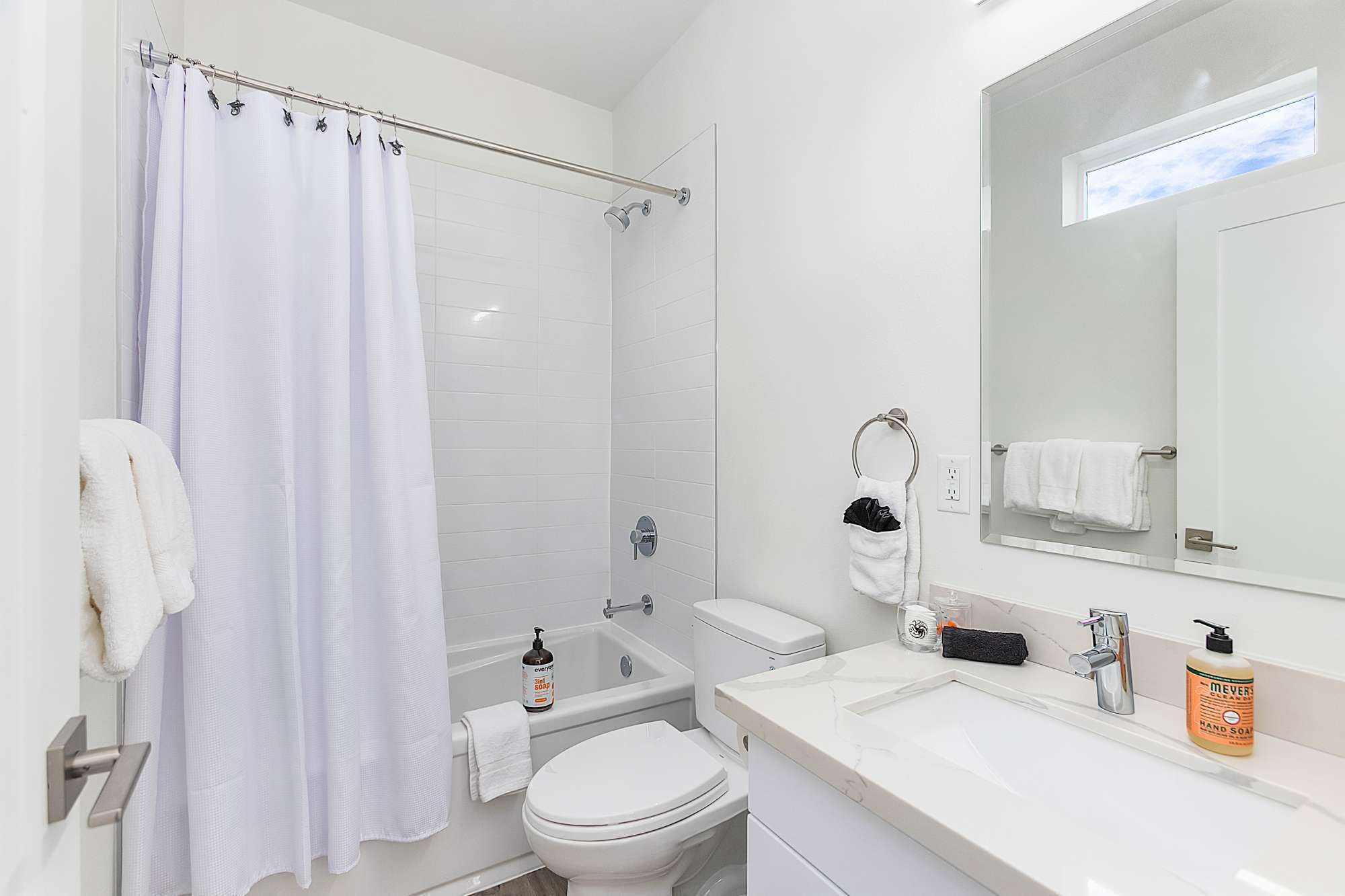 Un baño moderno con cabina de ducha de vidrio, inodoro, lavabo con espejo y artículos de aseo.