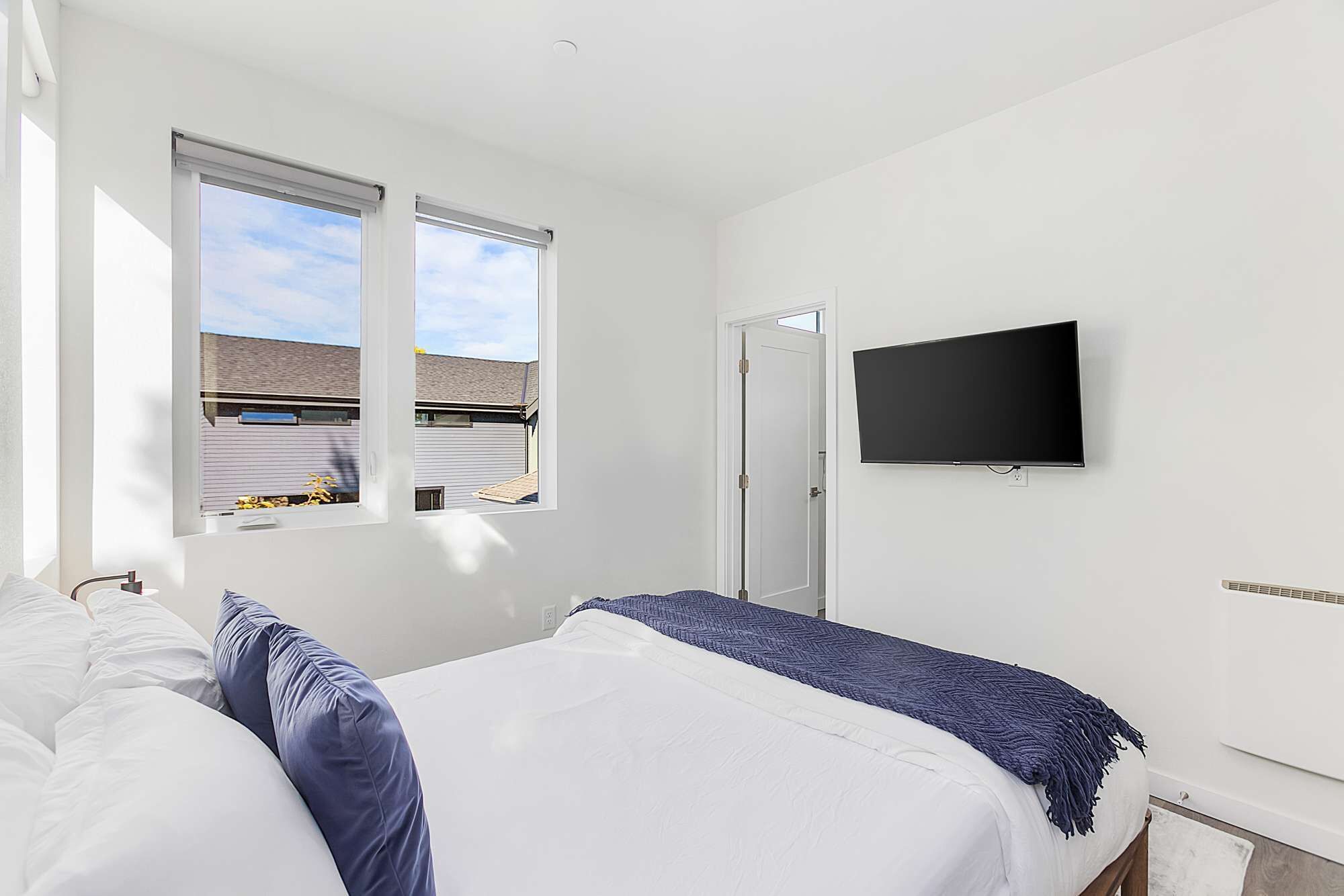 Ein Schlafzimmer mit zwei Betten, einem Fernseher und einem Fenster mit Blick auf ein Gebäude.