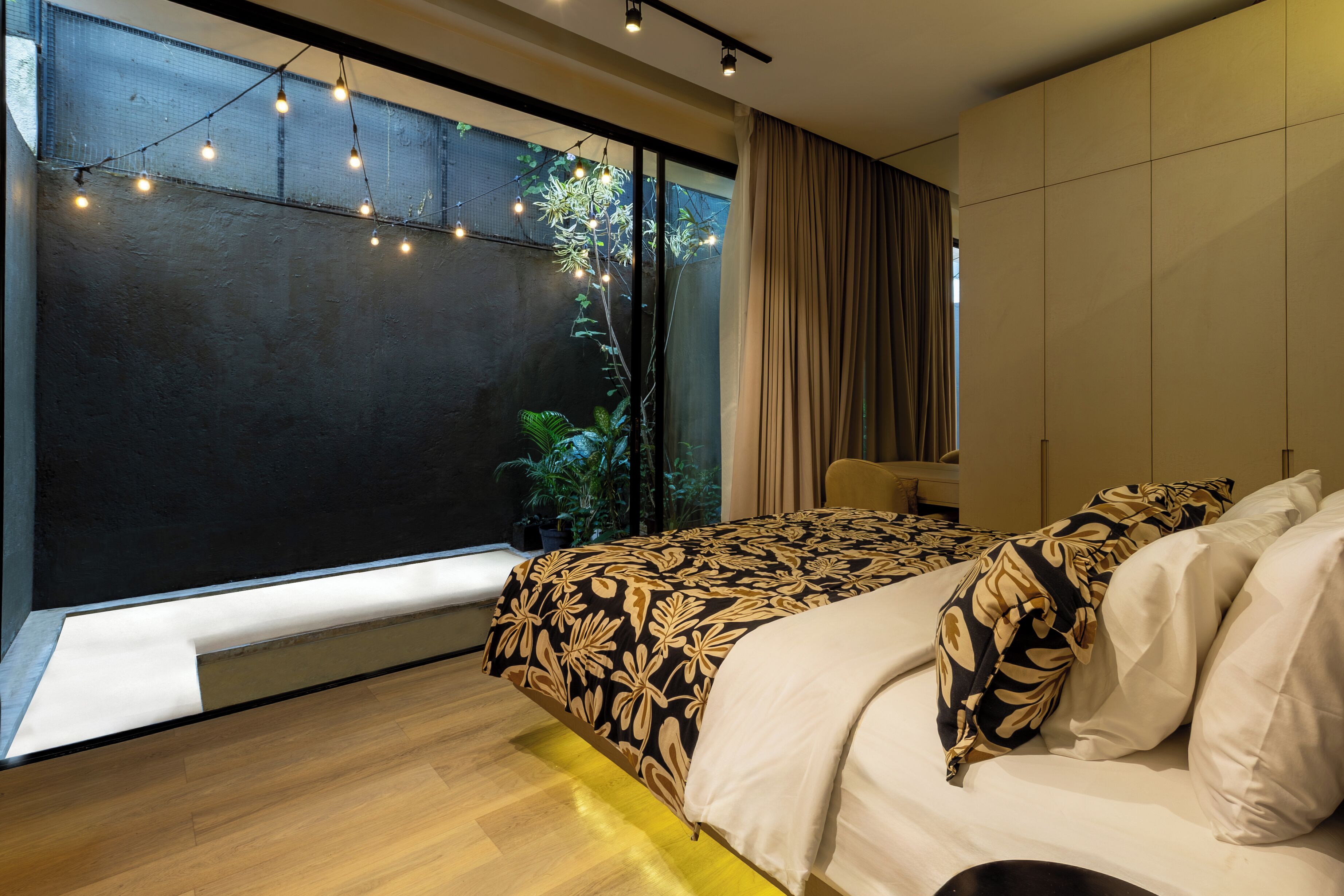 A modern bedroom with a large window, a bed with patterned bedding, and a bedside table.