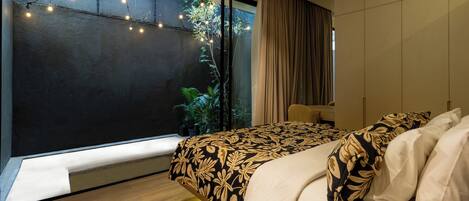 A modern bedroom with a large window, a bed with patterned bedding, and a bedside table.