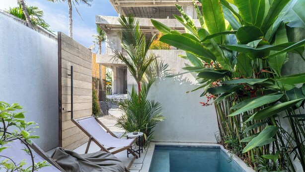 A small outdoor pool area with two lounge chairs and a small table, surrounded by lush tropical plants. - Oasis Villa 9 by Betterplace (Canggu)