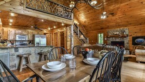 Interior de una cabaña de madera con comedor, cocina y chimenea, incluyendo un hogar de piedra.