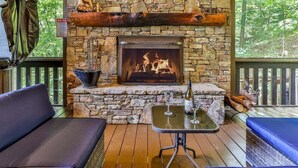 Una chimenea de piedra con fuego, una mesa con copas y botellas, y dos sofás.