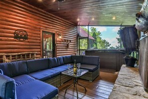 A log cabin with a blue sofa, a small table with a bottle and glasses, and a view of the outdoors. - Sunrise Overlook | Blue Ridge, GA (Blue Ridge)
