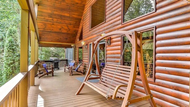 Una cabaña de troncos con terraza de madera, asientos exteriores y una hamaca.