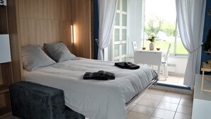 Ein Schlafzimmer mit einem Bett, einer Bank, einem kleinen Tisch mit einer Vase und Blick ins Freie.