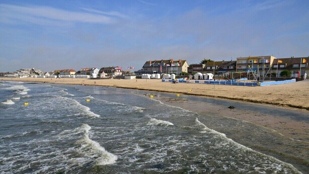 Ein Strand mit Wellen, einem sandigen Ufer und Gebäuden im Hintergrund.