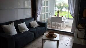 Ein dunkelbraunes Sofa mit zwei Kissen, ein weißer Couchtisch mit einer Schale und Blick auf einen Garten durch eine Glastür.