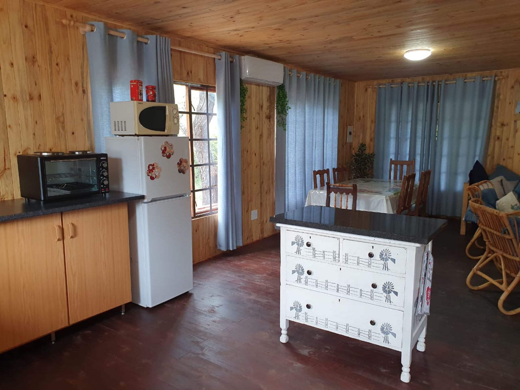 A wooden-paneled kitchen with a microwave, refrigerator, and a small dining table with chairs.