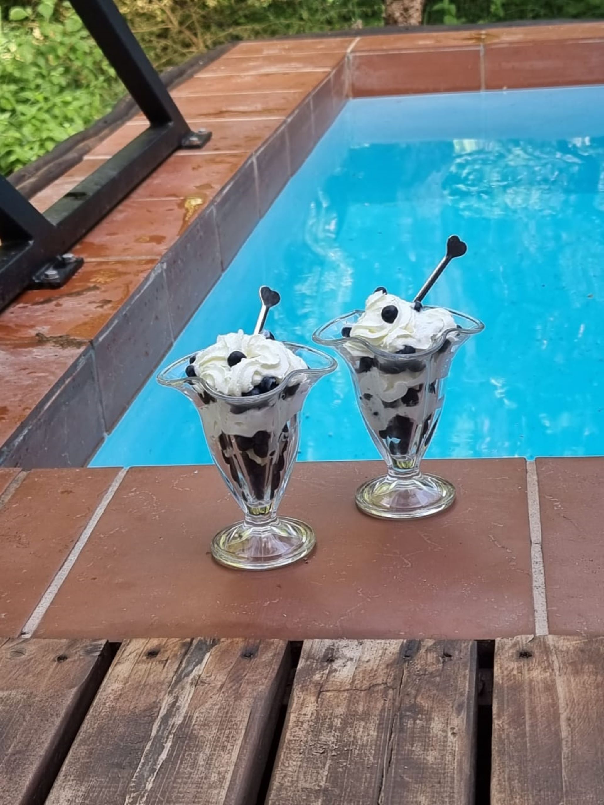 Deux coupes à parfait sur une table en bois, près d’une piscine.