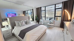 Una habitación de hotel moderna con una cama grande, un escritorio, una silla, un televisor y una ventana con cortinas.