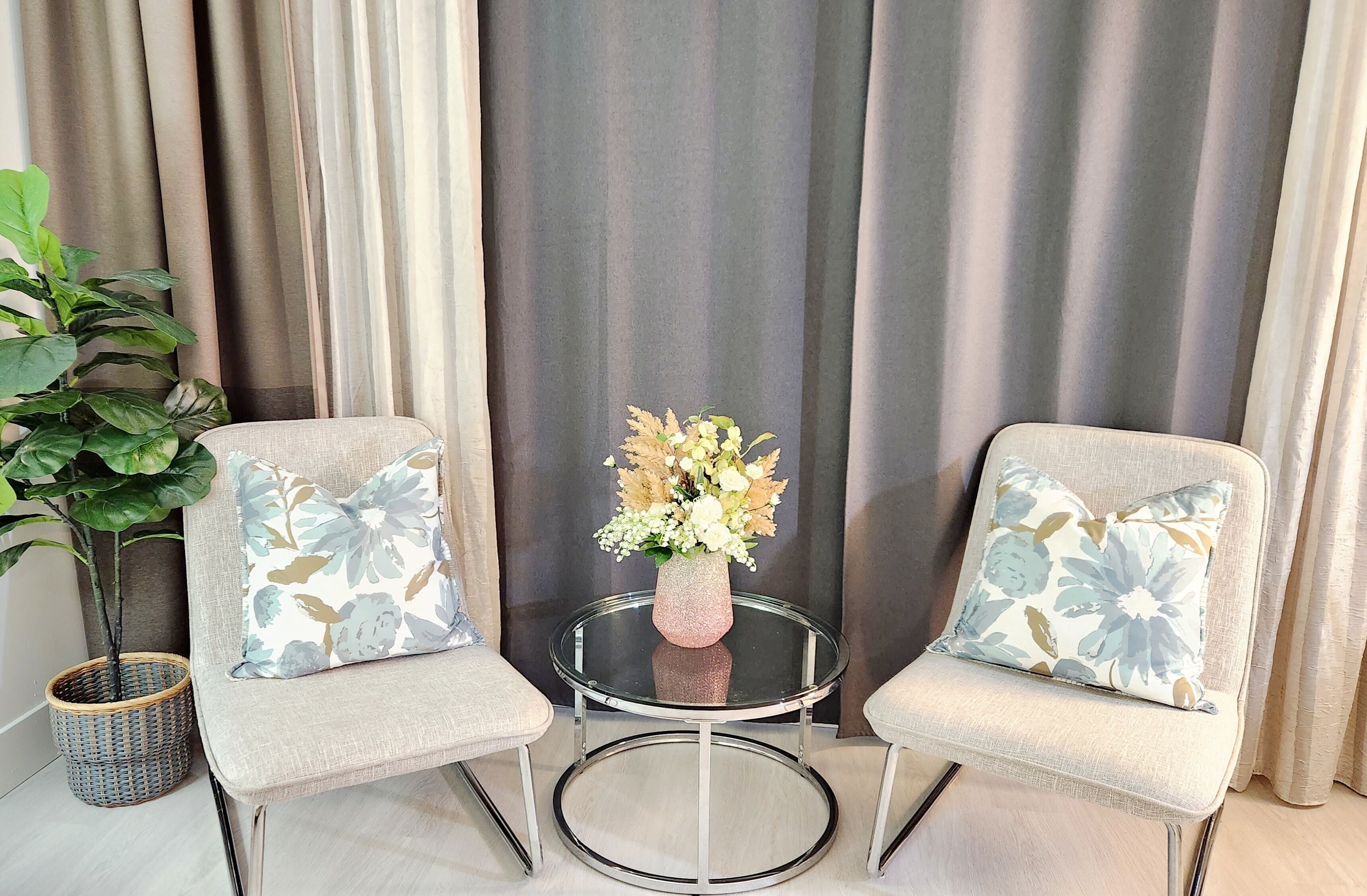 Ein Zimmer mit zwei Sesseln, einem kleinen runden Tisch mit Blumenvase und einer Topfpflanze.