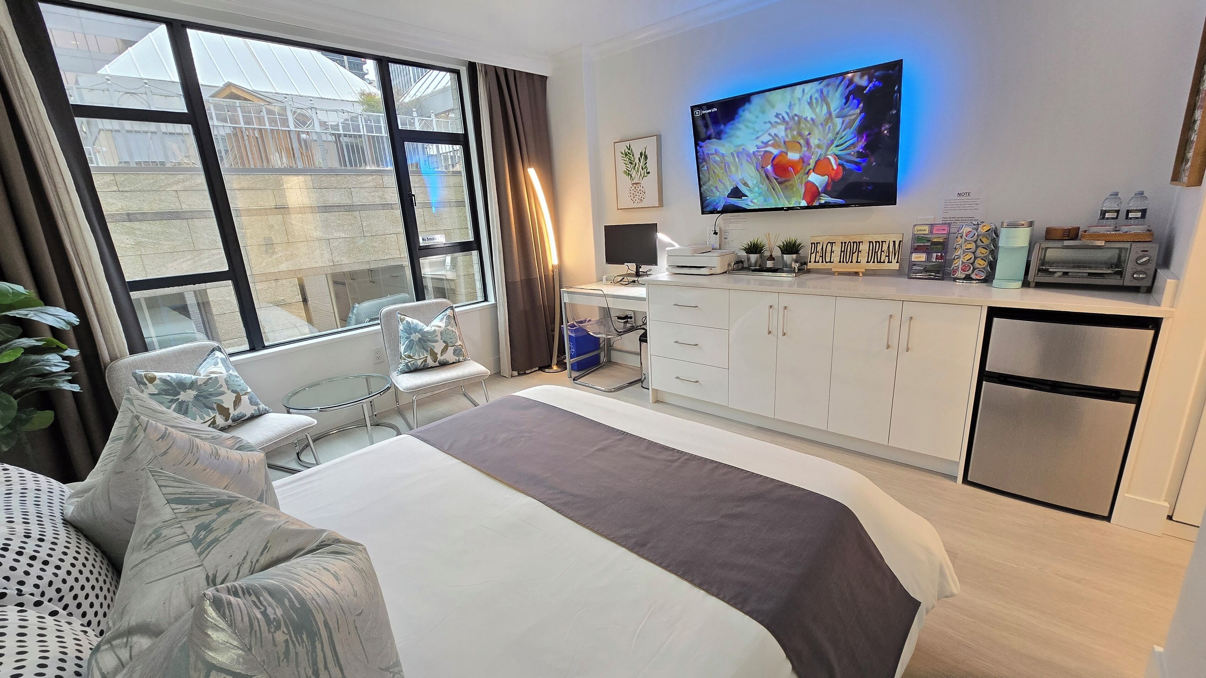 Habitación de hotel moderna con una cama grande, un escritorio con computadora, televisor de pantalla plana y una kitchenette.