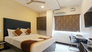 A hotel room with a bed, a desk, a chair, a ceiling fan, and an air conditioning unit. - Manjhi Residency  (Tiruchirappalli)