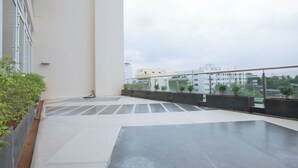 A spacious balcony with a tiled floor, potted plants, and a view of buildings in the background. - Manjhi Residency  (Tiruchirappalli)