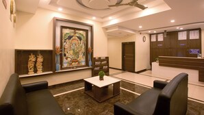 A hotel lobby with a reception desk, seating area, artwork, and a ceiling fan. - Manjhi Residency  (Tiruchirappalli)