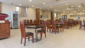 A spacious dining area with multiple wooden tables and chairs, a refrigerator, and a water dispenser. - Manjhi Residency  (Tiruchirappalli)