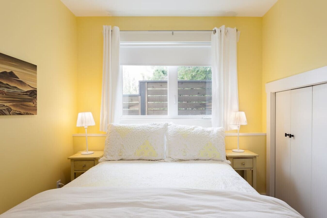 Una camera da letto con un letto, due lampade ai lati, una finestra con tende e una porta.