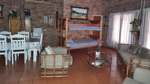 A rustic room with a brick wall, a wooden bunk bed, a sofa, a dining table with chairs, and a television mounted on the wall. - Klein Huisie Little House Self Catering Africa Bush Vacation In Marloth Park (Nkomazi)