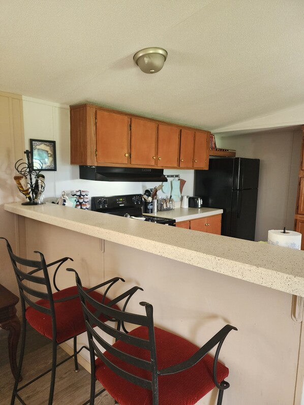 A kitchen with wooden cabinets, a black refrigerator, a countertop with a stove, and two red chairs.