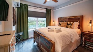 A bedroom with a wooden bed, green curtains, a ceiling fan, and a window with a view of greenery. - Modern 1BR Flat: Free Parking, AC, Getaway Ready! (Lynchburg)