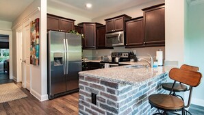 A modern kitchen with dark wood cabinets, stainless steel appliances, and a granite island with bar stools. - Modern 1BR Flat: Free Parking, AC, Getaway Ready! (Lynchburg)