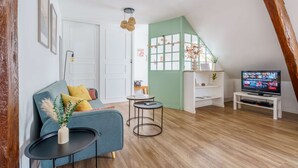 Ein gemütliches Wohnzimmer mit einem blauen Sofa, einem kleinen runden Tisch, einem Fernseher auf einem Schrank und einer grünen Akzentwand.