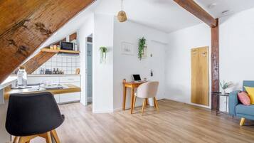 A modern loft apartment with exposed wooden beams, a kitchen with a microwave, a dining area with a table and chairs, and a living room with a sofa and a blue armchair.
