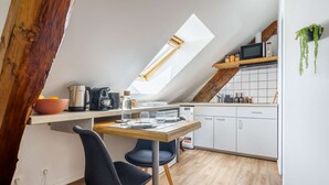 Eine kompakte Küche mit Essbereich, ausgestattet mit einem Holztisch, zwei schwarzen Stühlen, einer Kaffeemaschine und einer Mikrowelle.