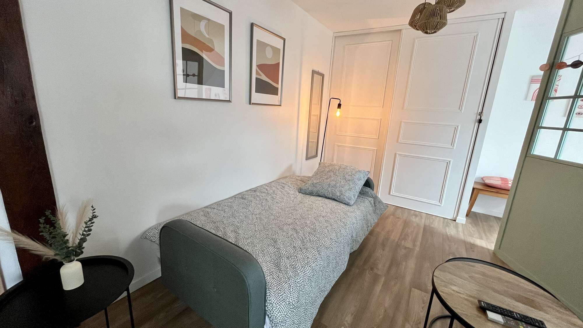 Ein kleines, ordentlich eingerichtetes Schlafzimmer mit einem Einzelbett, einem Nachttisch, einem Stuhl und einem Tisch mit einer Fernbedienung.