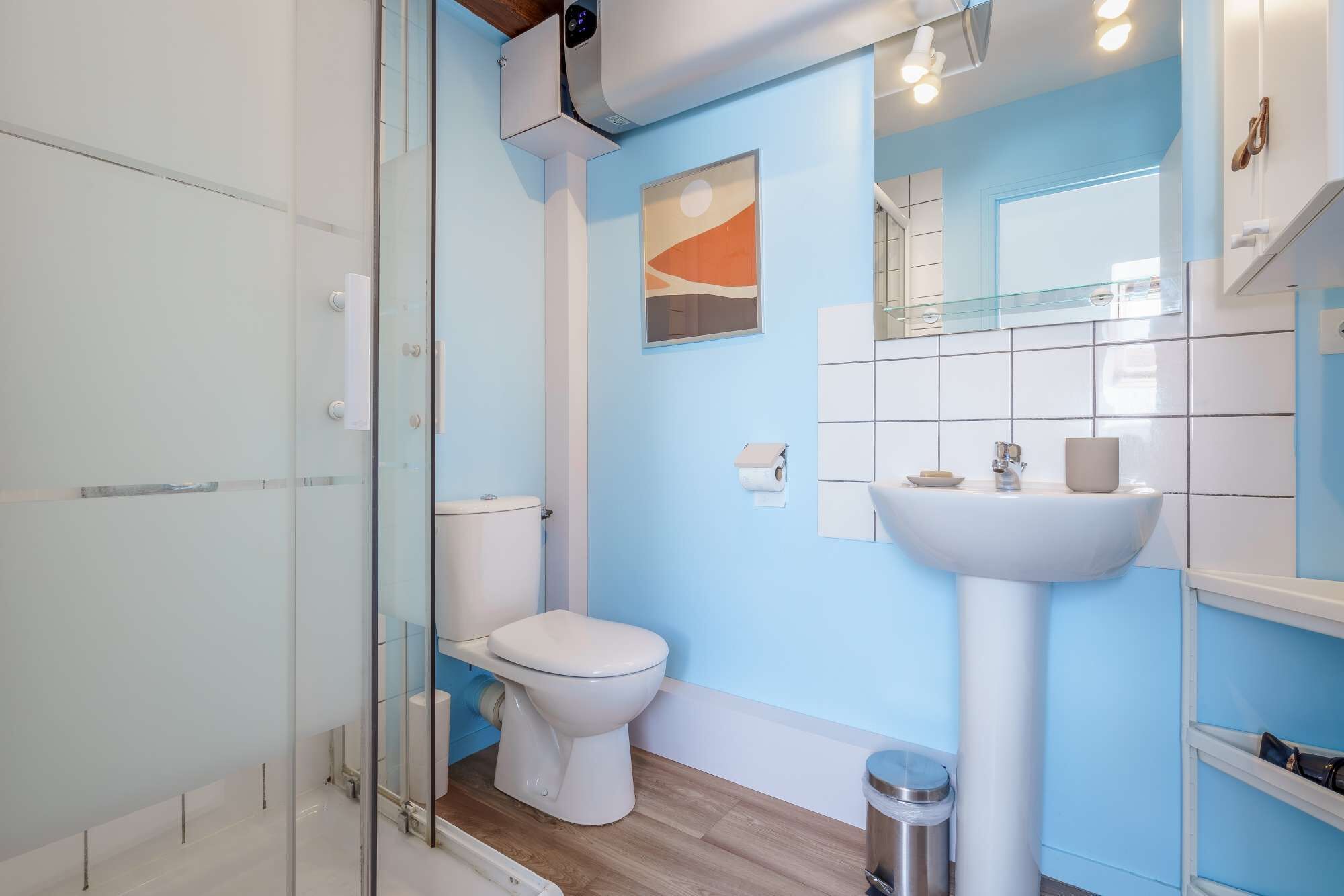 Et moderne badeværelse med et glasbadeværelse, et hvidt toilet og en vask med et spejl over.