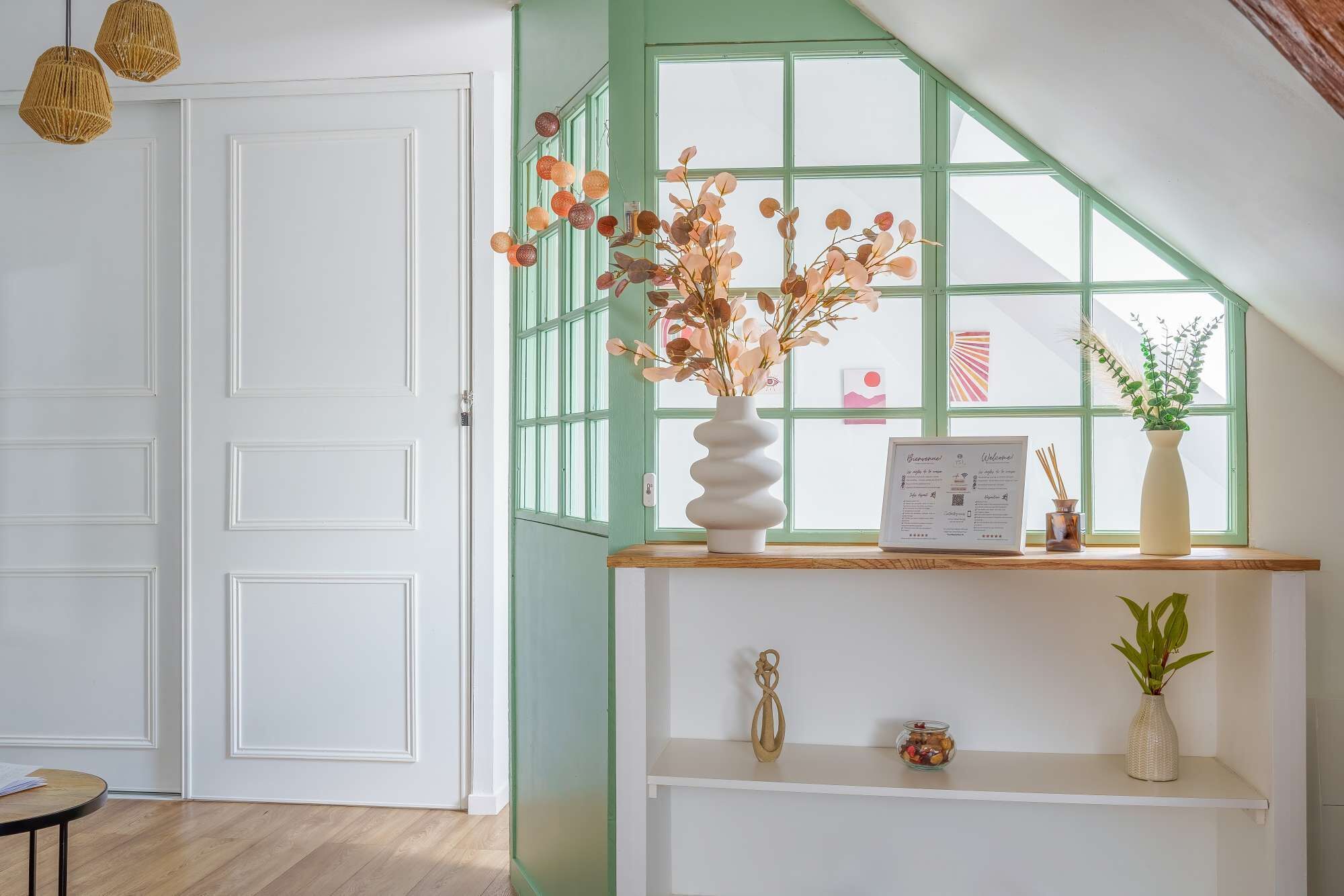 A room with a white door, a green window, and a wooden shelf with decorative items.