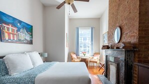 Quarto de hotel com cama, ventilador de teto, lareira, um quadro e vista da cidade pela janela.